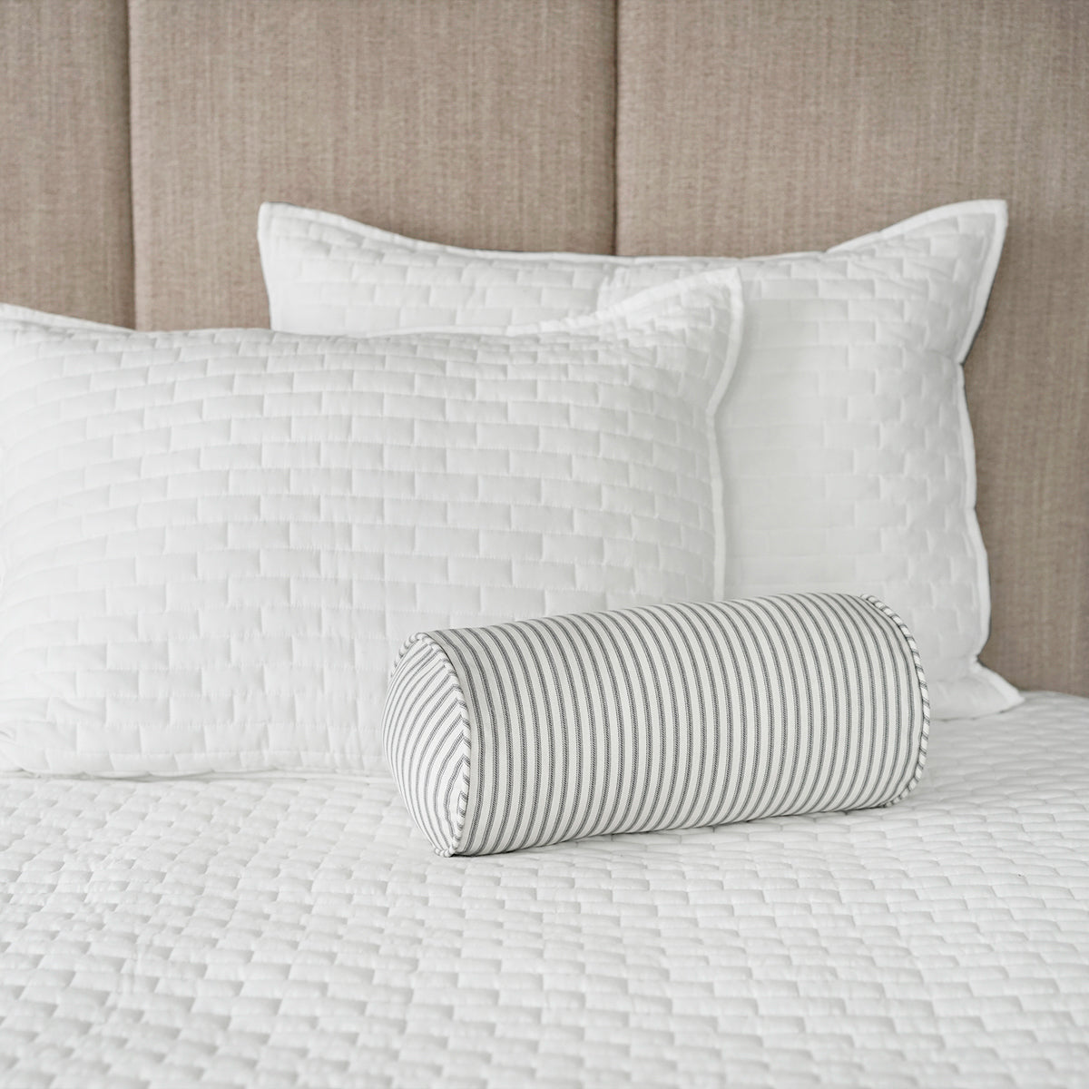 Gray Ticking Stripe Bolster Pillow Shown On Bed with White Bedding and Linen Headboard